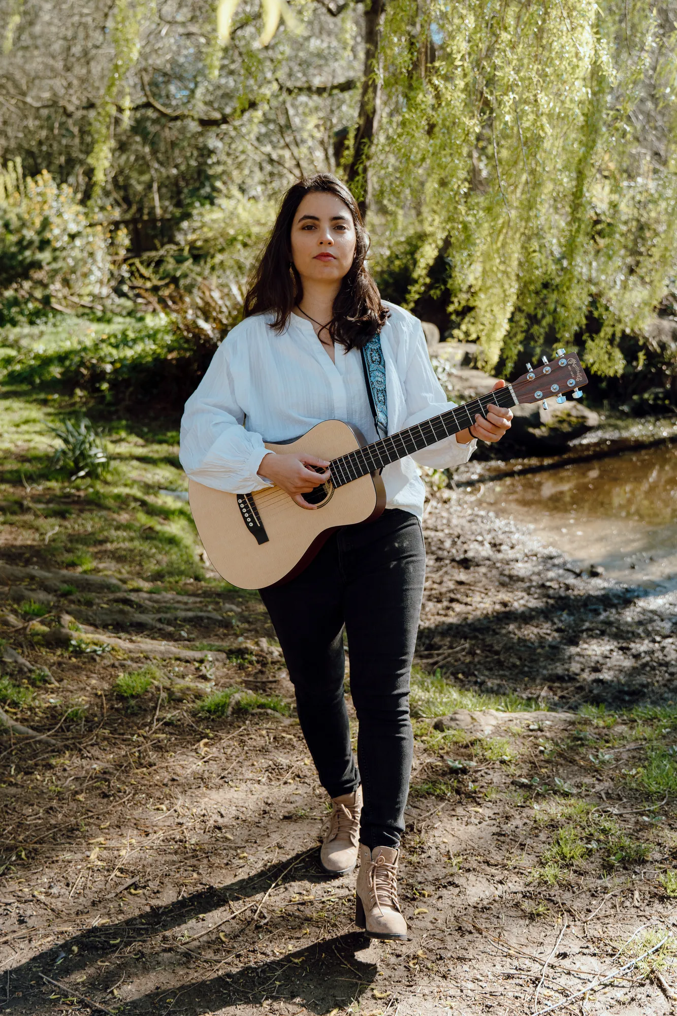 Ani walking along the riverbank playing her guitar