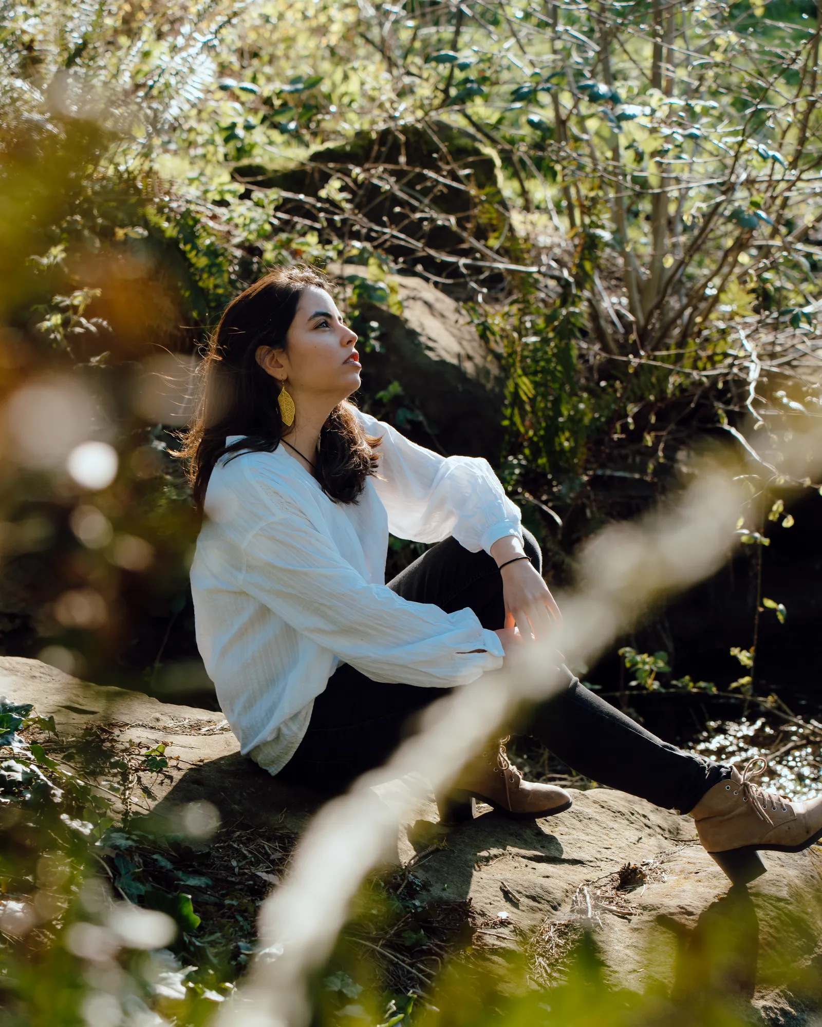 Ani sitting on a rock in the woods, looking up at the trees
