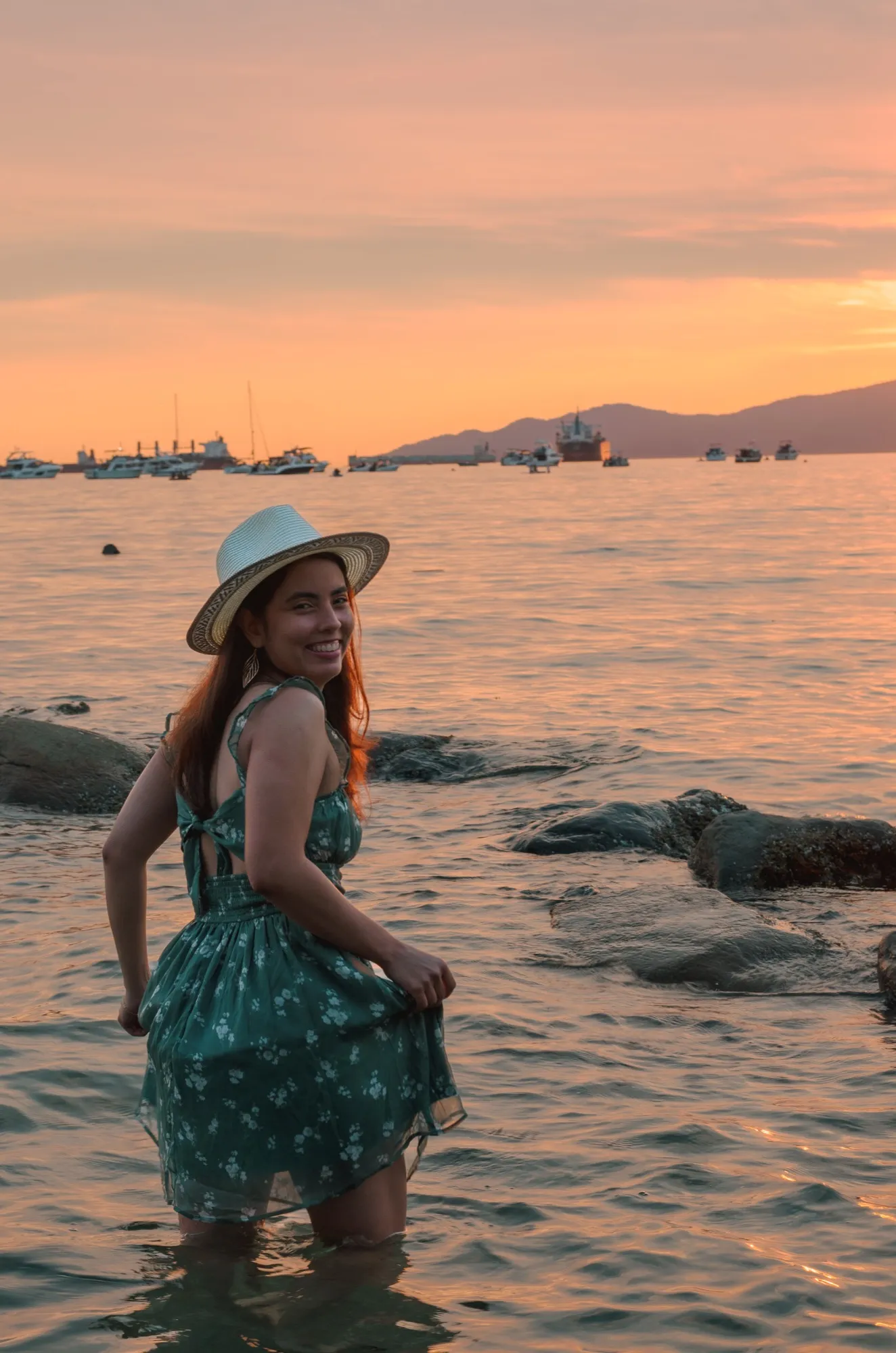 Ani smiling over her shoulder while wading in the sea at sunset
