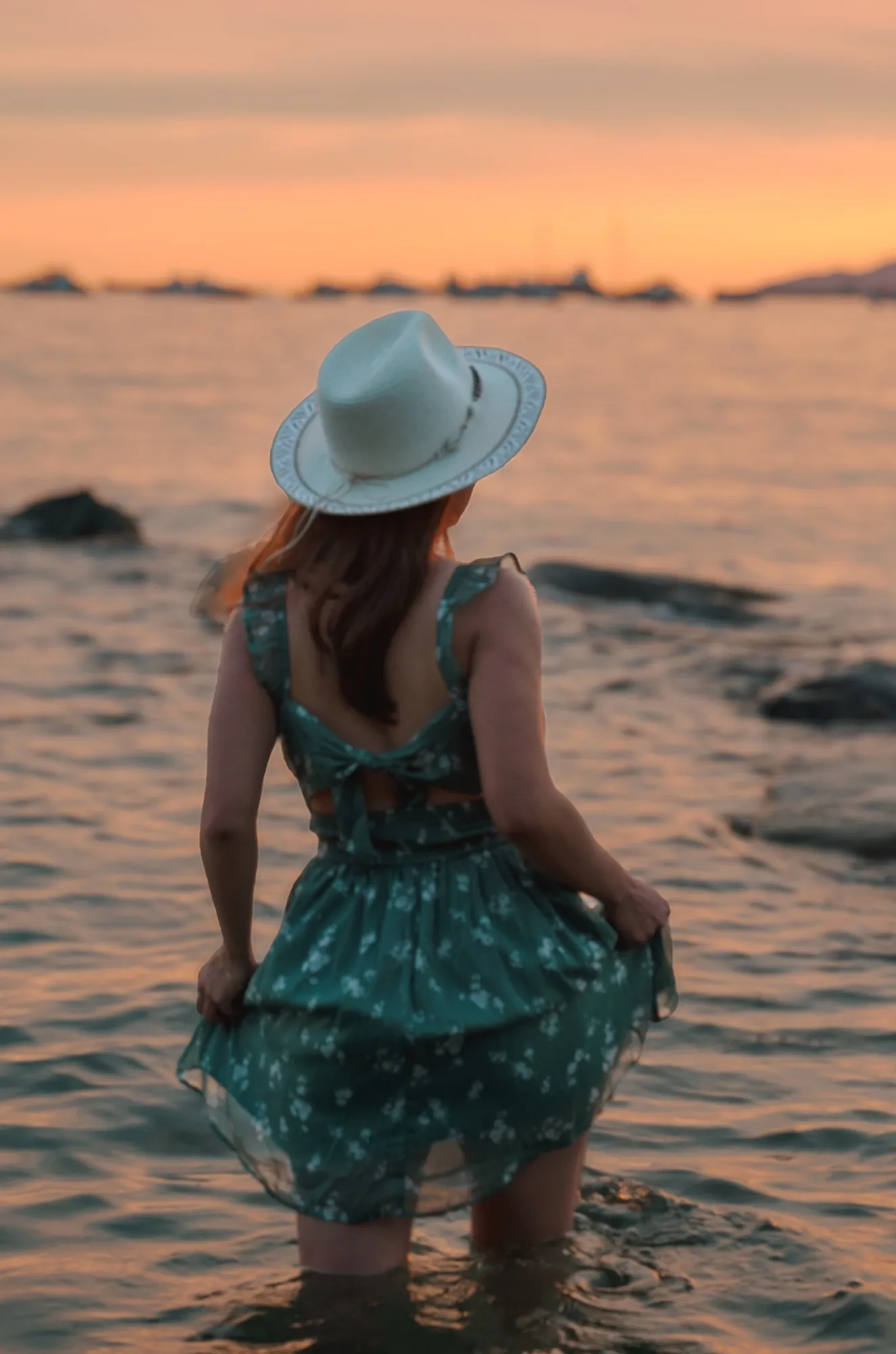 Ani in a straw hat wading into the sea at dusk