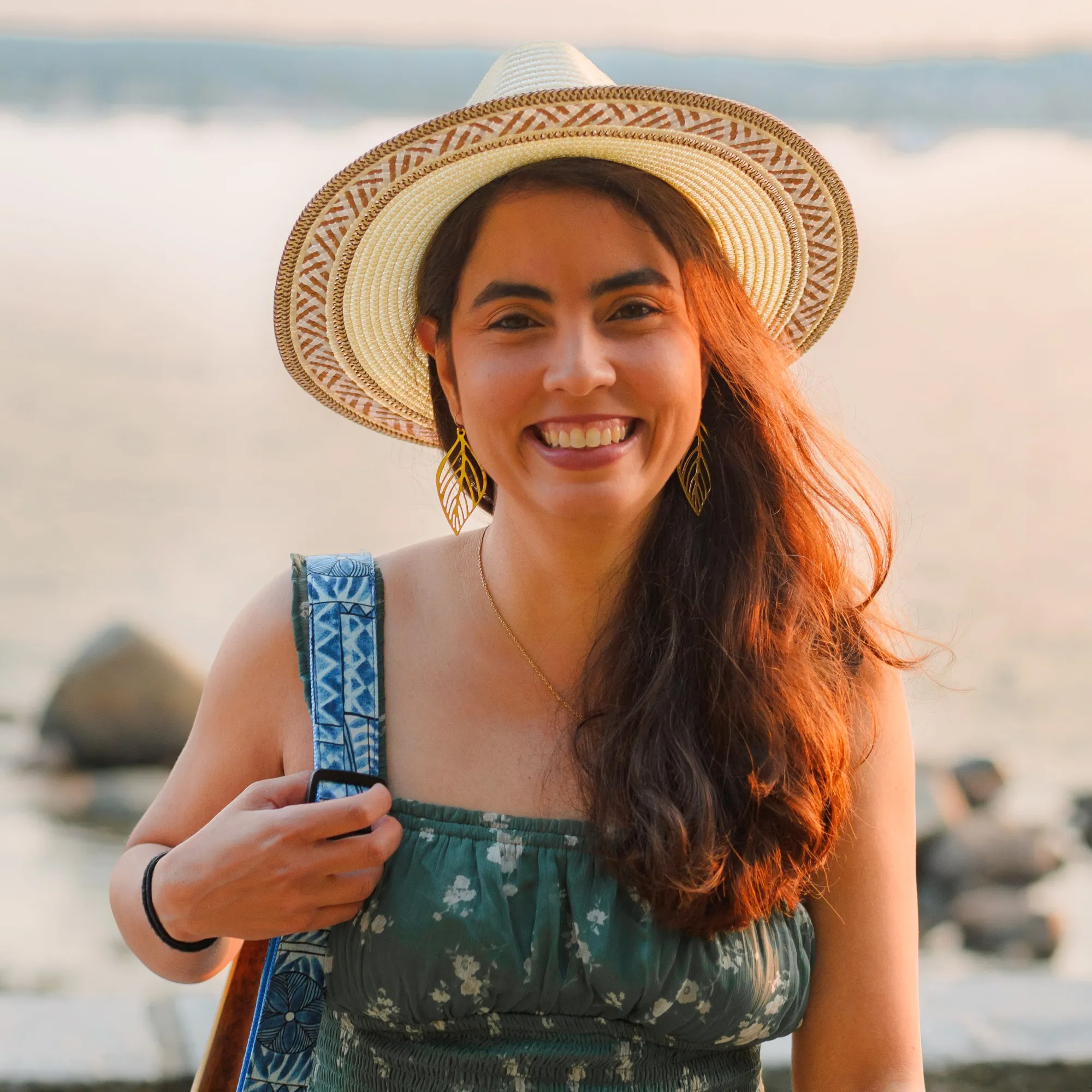 Ani smiling in a straw hat at golden hour by the water