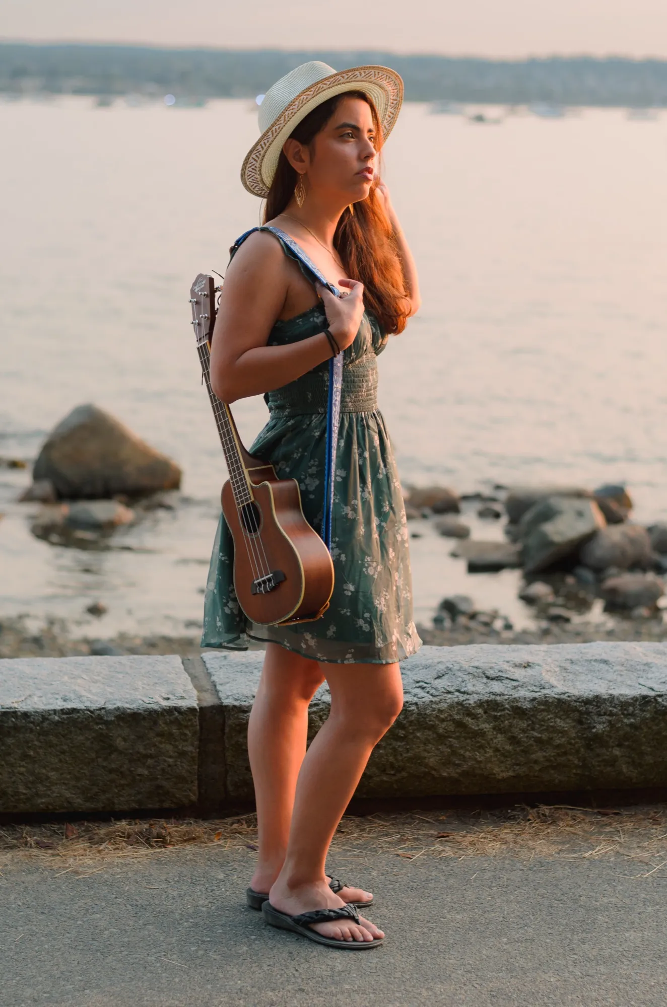 Ani standing on the seawall with her ukulele, looking out to sea