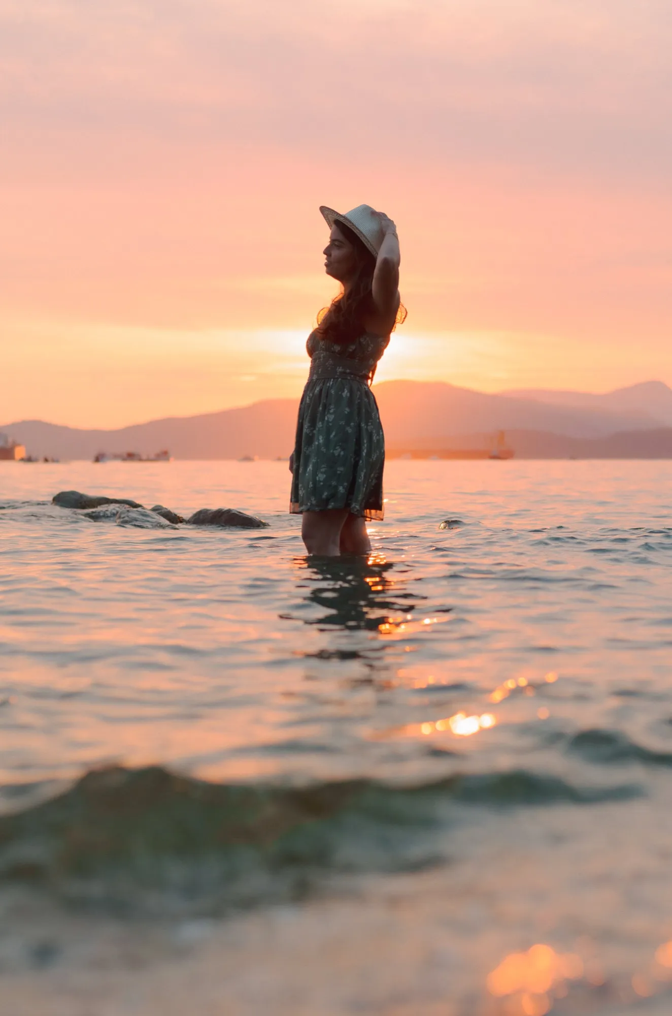 Ani standing in the sea against a pink sunset sky
